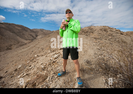 Determined senior man holding water bottle while standing on mountain Stock Photo