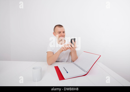 Smiling businessman text messaging on cell phone at desk Stock Photo