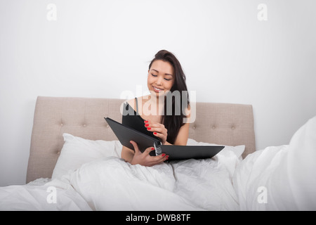 Happy young woman with spiral notepad in bedroom Stock Photo