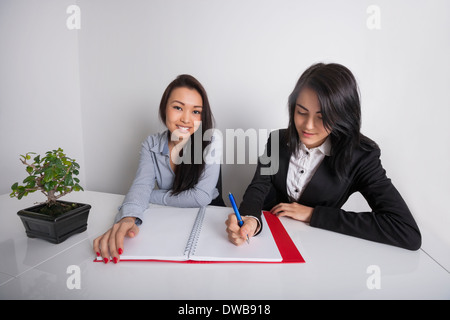 Portrait of happy businesswoman with colleague writing in spiral notebook at office desk Stock Photo