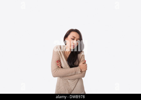 Young woman with arms crossed shivering against gray background Stock Photo