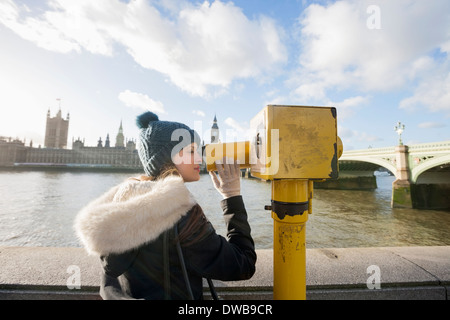 Side view of young woman looking through telescope by river Thames, London, UK Stock Photo