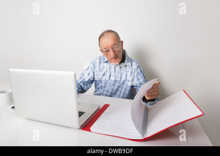 Senior businessman using laptop while reading file at office desk Stock Photo