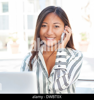 Portrait of an asian woman in font of a laptop and talking on phone Stock Photo