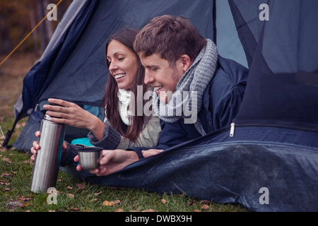 Happy young couple with thermos lying in tent at forest Stock Photo