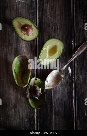 Spoon and sliced and hollowed halfs of two avocados on wooden table Stock Photo