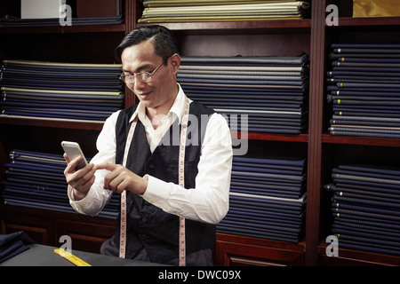 Tailor texting on cellphone in tailors shop Stock Photo