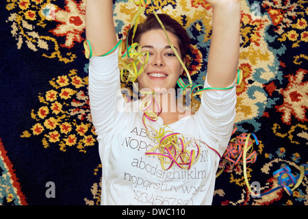 Portrait of young woman and streamers lying on patterned rug Stock Photo