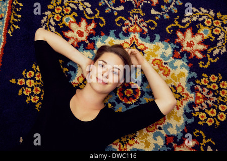 Portrait of young woman lying on patterned rug Stock Photo