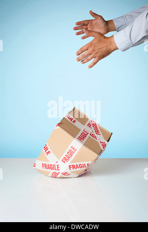 Studio shot of hands dropping cardboard box marked fragile Stock Photo
