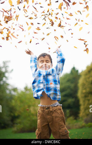Male toddler in the garden throwing up autumn leaves Stock Photo