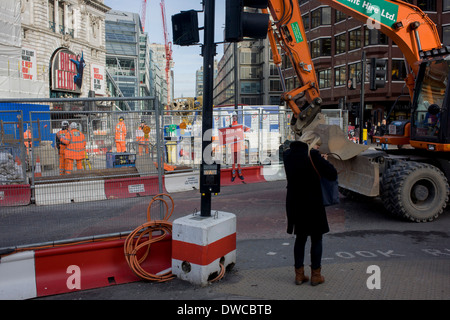 Digger drives past footpath disruption sign using illustration of TFL workman. Stock Photo