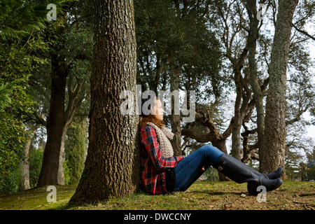 Teenage girl sitting against tree in forest Stock Photo