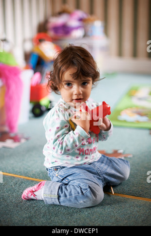 Female toddler sitting on playroom floor playing with a red toy Stock Photo