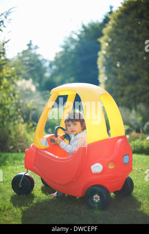Female toddler playing in toy car in the garden Stock Photo