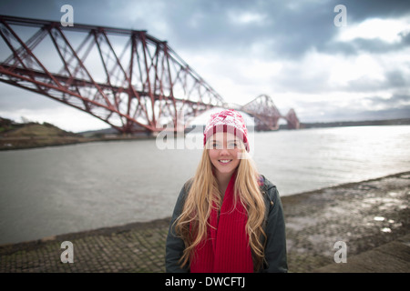 A young womans poses in front of the Forth Rail Bridge in Queensferry, near Edinburgh, Scotland Stock Photo