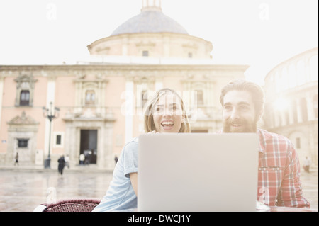 Young couple looking at laptop in sidewalk cafe, Plaza de la Virgen, Valencia, Spain Stock Photo