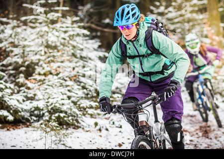 Two female mountain bikers riding through forest in snow Stock Photo