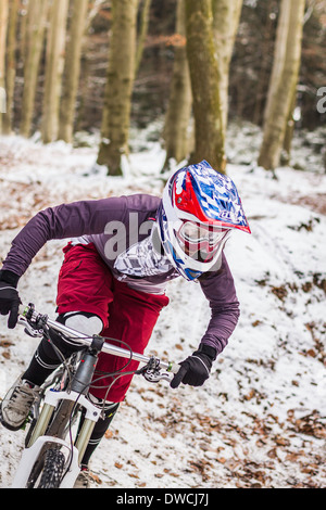 Young female mountain biker riding downhill through forest Stock Photo