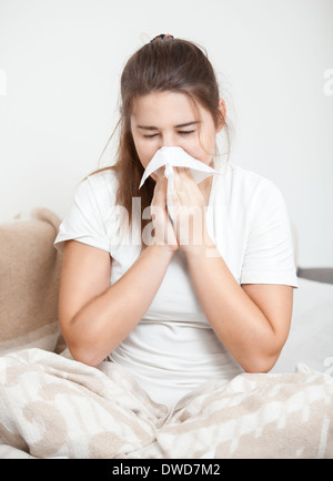 Brunette woman sitting on bed and sneezing Brunette woman sitting on bed and sneezing