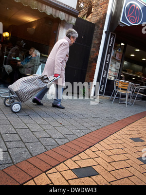 An elderly senior woman pulling a shopping trolley on a uk high street Stock Photo