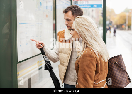 Young couple reading time table on bus stop Stock Photo