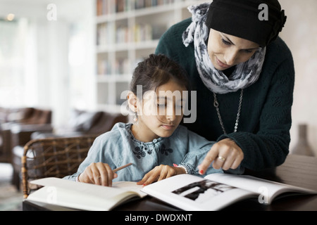 Mother assisting girl in doing homework at table Stock Photo