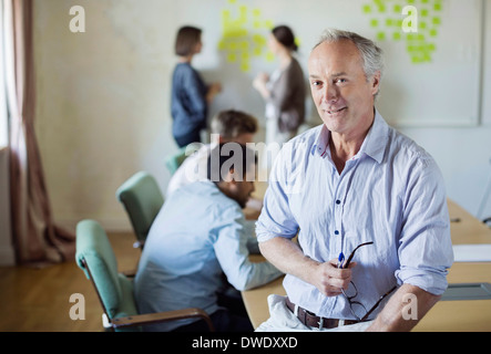 Portrait of confident businessman sitting on conference table with colleagues discussing in background Stock Photo