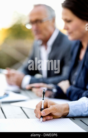 Cropped image of businessman writing on document with colleagues at table Stock Photo