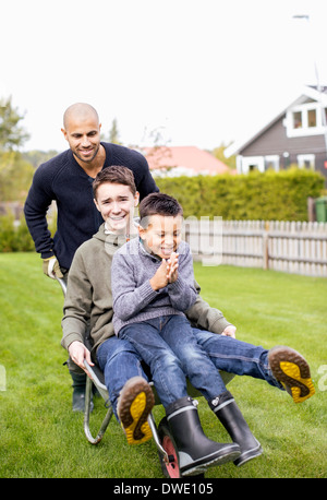 Father pushing children in wheel barrow at yard Stock Photo