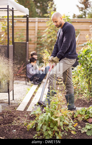 Man digging in garden with children in background Stock Photo