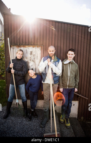 Portrait of confident family with gardening equipment standing against house Stock Photo