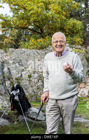 Portrait of happy senior man holding golf ball and club in yard Stock Photo