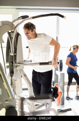 Man exercising on pull-up assist machine at gym Stock Photo