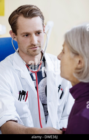 Male doctor checking senior woman's heart with stethoscope in clinic Stock Photo