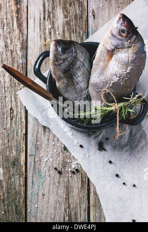 Top view on tow raw dorado fish with rosemary and sea salt server in black pan over old wooden table. See series Stock Photo