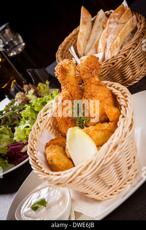 Crisp crunchy golden chicken legs and wings deep fried in bread crumbs and served with a bowl of dip in a wicker basket for a delicious appetizer Stock Photo
