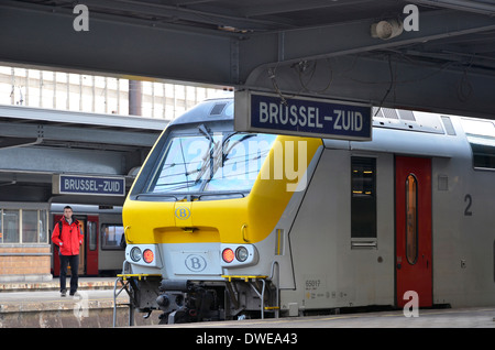 Regional train standing at Brussels-Zuid (Brussels-South) railway station withpassenger in red coat on opposite platform. Stock Photo