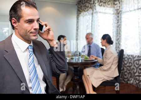Businessman using cellphone with colleagues having meal Stock Photo