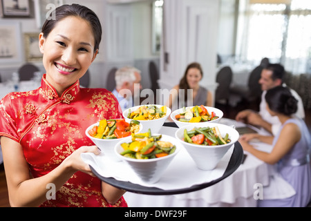 Waitress carrying food tray with people at dining table in restaurant Stock Photo