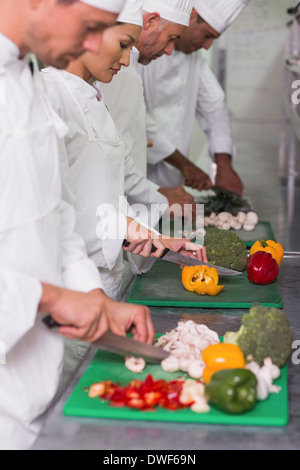 Row of trainee chefs slicing vegetables Stock Photo