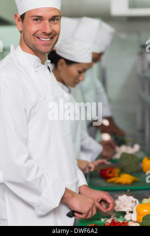 Row of trainee chefs slicing vegetables with one smiling at camera Stock Photo