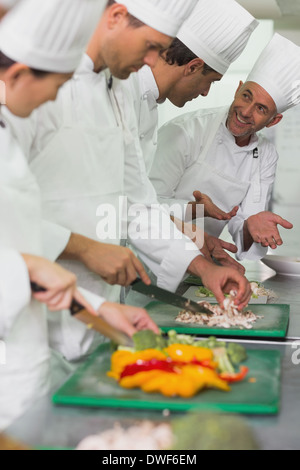 Row of trainee chefs slicing vegetables with tutor watching Stock Photo