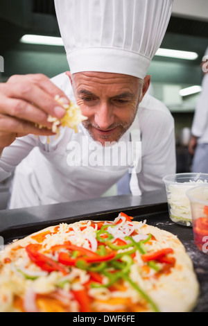 Happy chef sprinkling cheese on a pizza Stock Photo