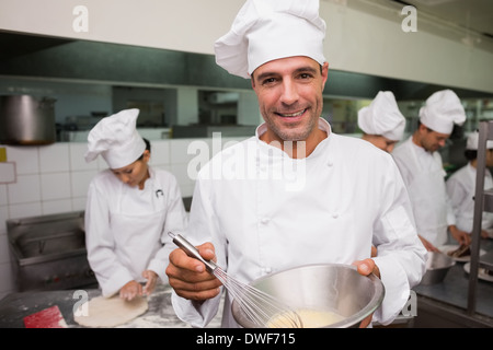 Happy chef whisking bowl of eggs smiling at camera Stock Photo