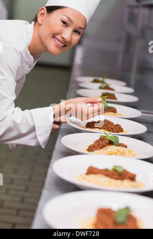 Happy chef putting basil leaf on spaghetti dish Stock Photo