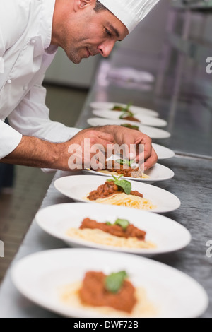 Happy chef putting basil leaf on spaghetti dish Stock Photo