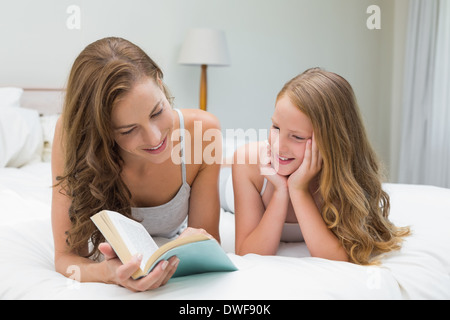 Girl and mother with book lying in bed Stock Photo