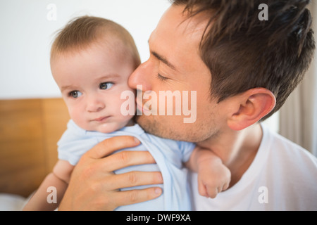 Father sitting on bed with baby son in blue babygro Stock Photo