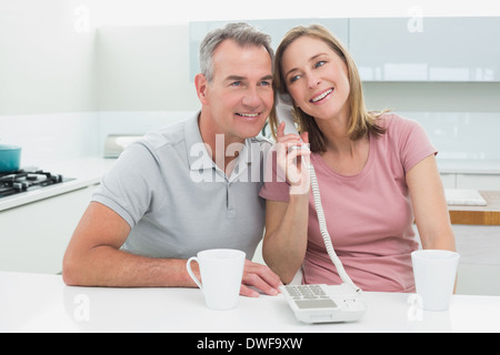 Happy couple using landline phone together in kitchen Stock Photo